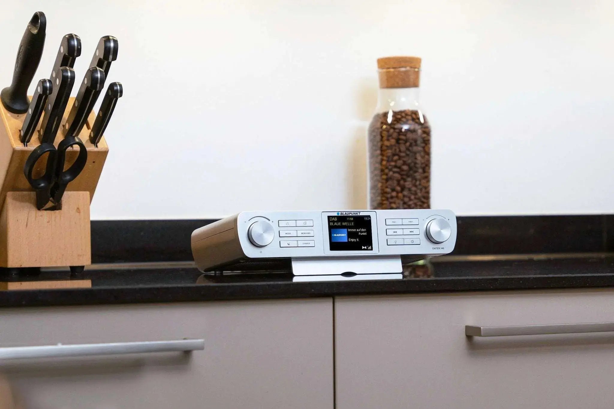 weißes Küchenradio mit DAB+ und Bluetooth auf Küchenarbeitsplatte neben Messerblock und Glasbehälter mit Kaffeebohnen
